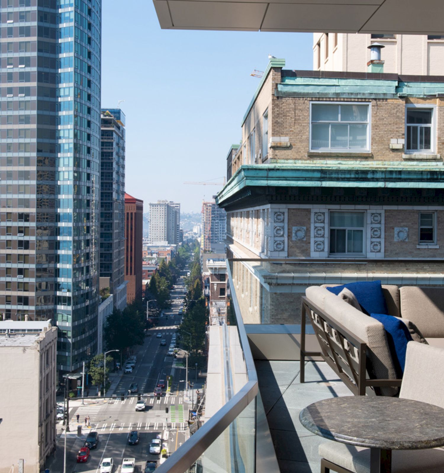 A cityscape with tall buildings, a busy street below, and a modern balcony featuring outdoor furniture including a table and cushioned seating.