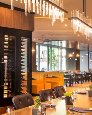 The image depicts an elegant restaurant interior with modern chandeliers, wine storage, and neatly set tables, ready for dining guests.