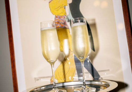 A framed picture shows a painting of a couple dancing, with two champagne flutes on a serving tray held by a hand.