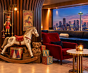 Vintage rocking horse, toy blocks and teddy bears beside a red velvet chair with the Seattle skyline and Space Needle at dusk